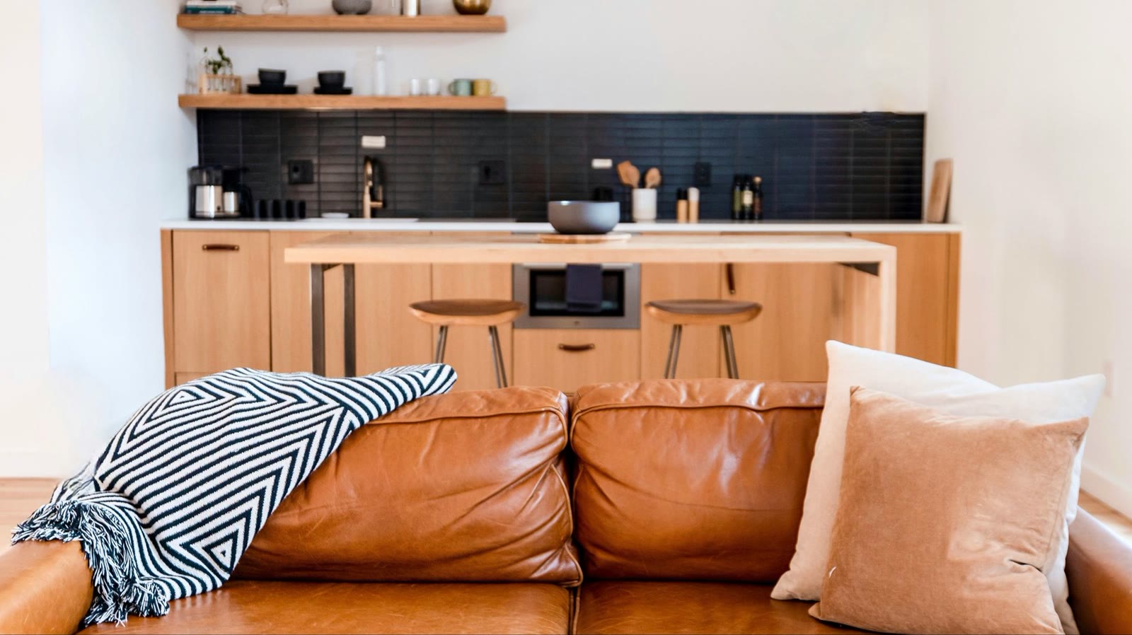 Bright living room with a leather sofa and an open-plan kitchen in a rental flat